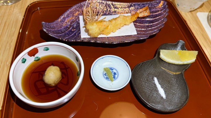 A beautifully plated dish featuring shrimp tempura served on a decorative purple plate, accompanied by dipping sauce, grated daikon, and a lemon wedge on a brown tray.