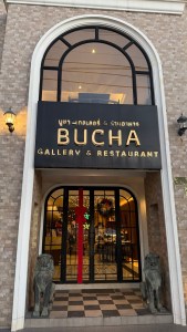 Exterior view of Bucha Gallery & Restaurant in Phuket, Thailand, featuring an elegant entrance with large glass doors and decorative stone lions flanking the entrance.