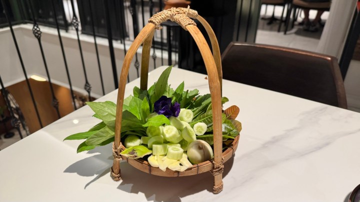 A traditional Thai selection of fresh vegetables and herbs, beautifully arranged in a bamboo basket, served as accompaniments to the meal.