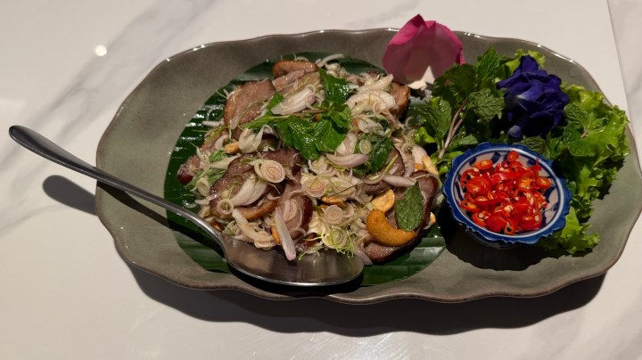 A colorful plate of Yam Takrai Ped, a duck and lemongrass salad served with fresh herbs, sliced shallots, and chilies on the side.