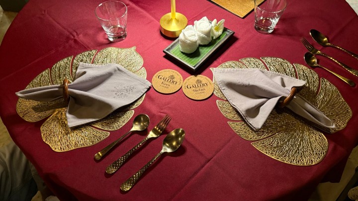 A beautifully set dining table at The Gallery Restaurant, featuring golden leaf-shaped placemats, elegant cutlery, and personalized coasters with the restaurant's logo.