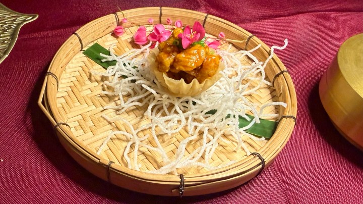 A delicate pastry filled with a savory mixture, garnished with colorful flowers, served on a traditional woven basket atop shredded coconut.