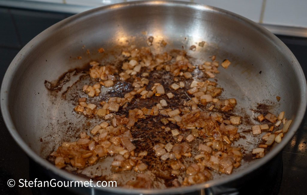 A stainless steel frying pan with caramelized chopped onions, showcasing a mix of browned and lightly burnt bits along the bottom.