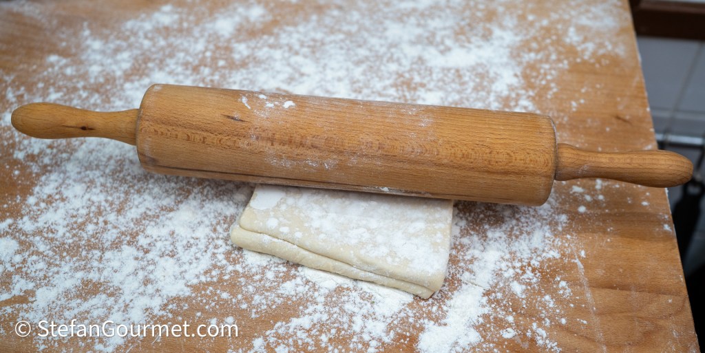 A wooden rolling pin resting on a sheet of dough on a floured wooden countertop.