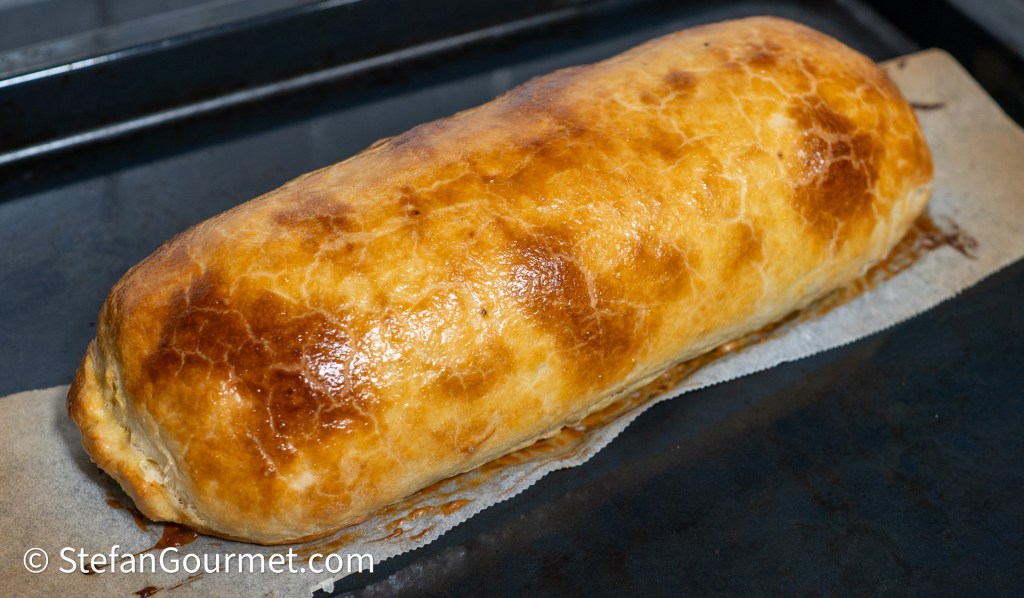 Golden-brown baked pastry loaf resting on a baking sheet, showcasing a flaky crust.