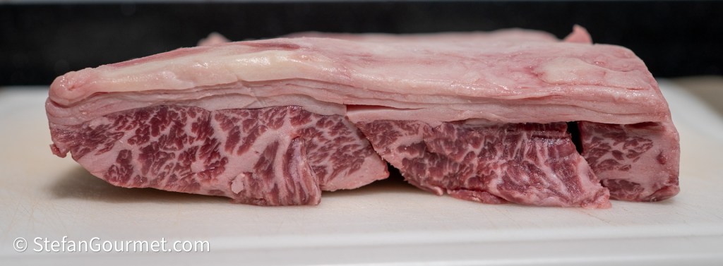 A raw piece of marbled beef with a visible fat cap, resting on a cutting board.