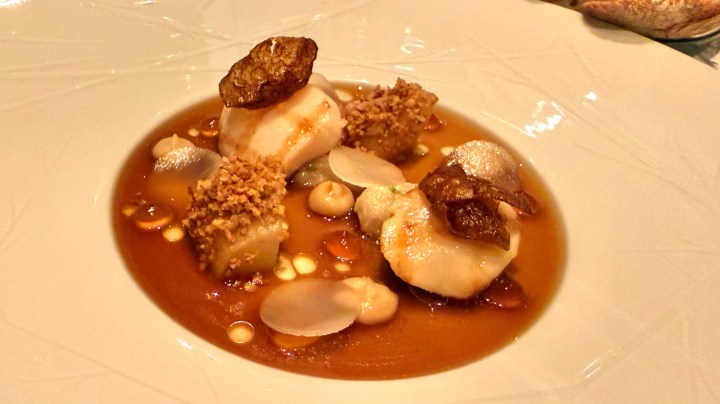 A beautifully plated dish featuring scallops, crunchy garnishes, and a rich sauce, served in a elegant white bowl.