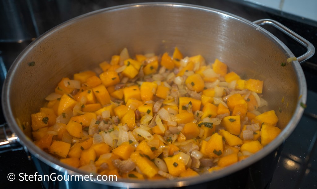 A pot on the stove filled with diced butternut squash and sautéed onions, cooking together until tender.