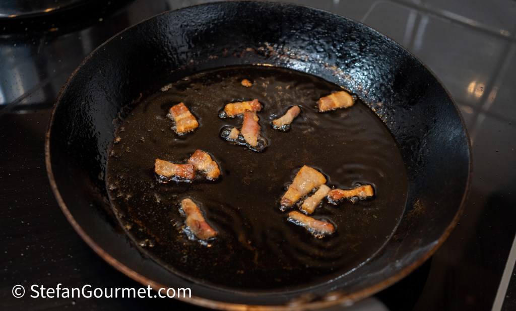 Cooked pieces of bacon sizzling in a frying pan with oil.