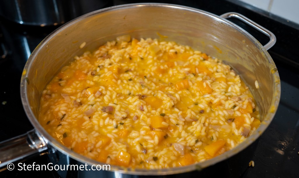 A pot of creamy risotto with chunks of butternut squash, cooked rice, and herbs on a stovetop.