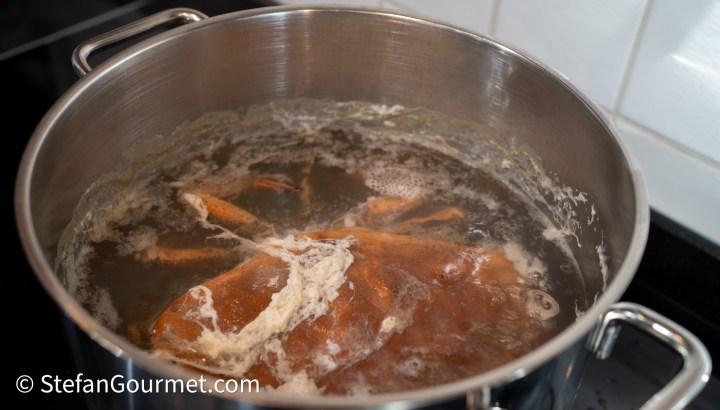 A large pot filled with boiling water and a cooked crab inside, with bubbles and steam visible.