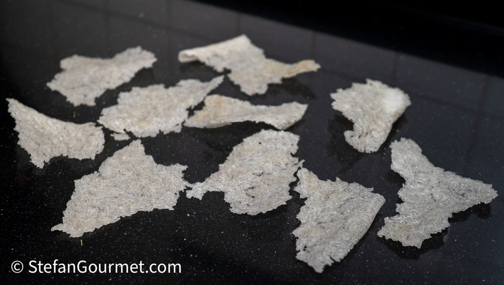 A collection of irregularly shaped, thin, translucent flakes displayed on a dark, glossy surface.