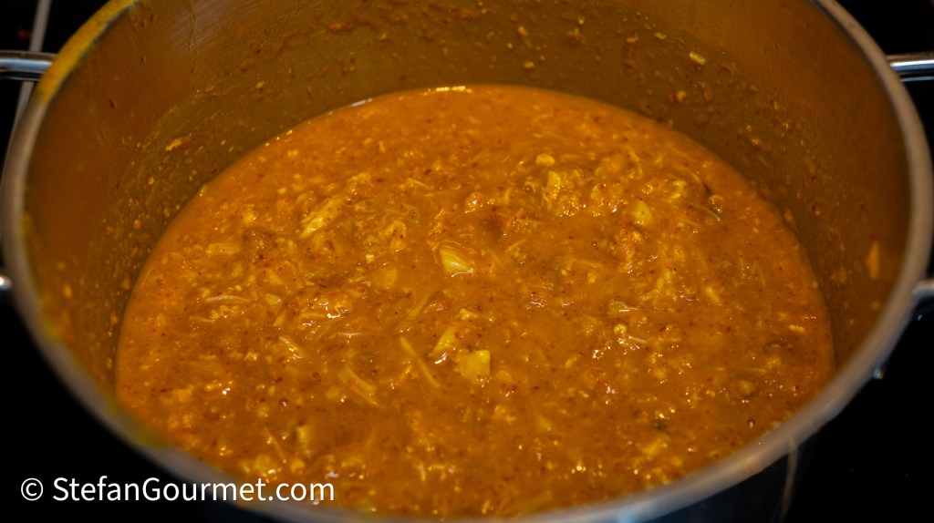 A pot filled with a thick, golden-brown curry mixture, bubbling gently on a stove, showcasing a rich texture with visible spices and ingredients.
