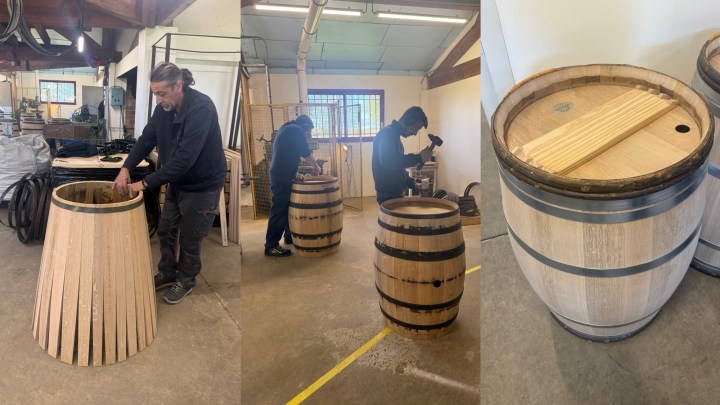 A craftsman assembling a wooden barrel using staves and metal bands.