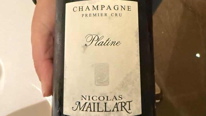A close-up of a bottle of Nicolas Maillart Champagne Premier Cru Platine, held in a hand.