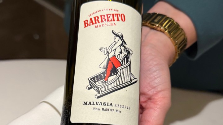 A close-up of a bottle of Barbeito Malvasia Reserva Madeira wine featuring a vintage-style label with an illustration of a man sitting in a chair.