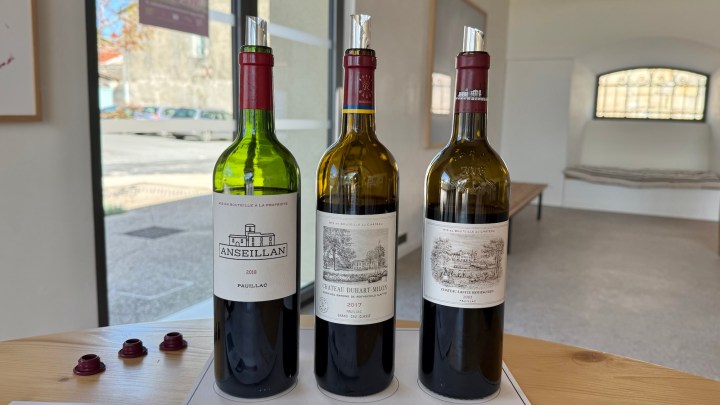 Three wine bottles displayed on a table, with labels showing different vintages: a green bottle labeled 'Anseillan 2020', a brown bottle labeled 'Château Durfort-Vivens 2017', and another brown bottle with a vintage design.