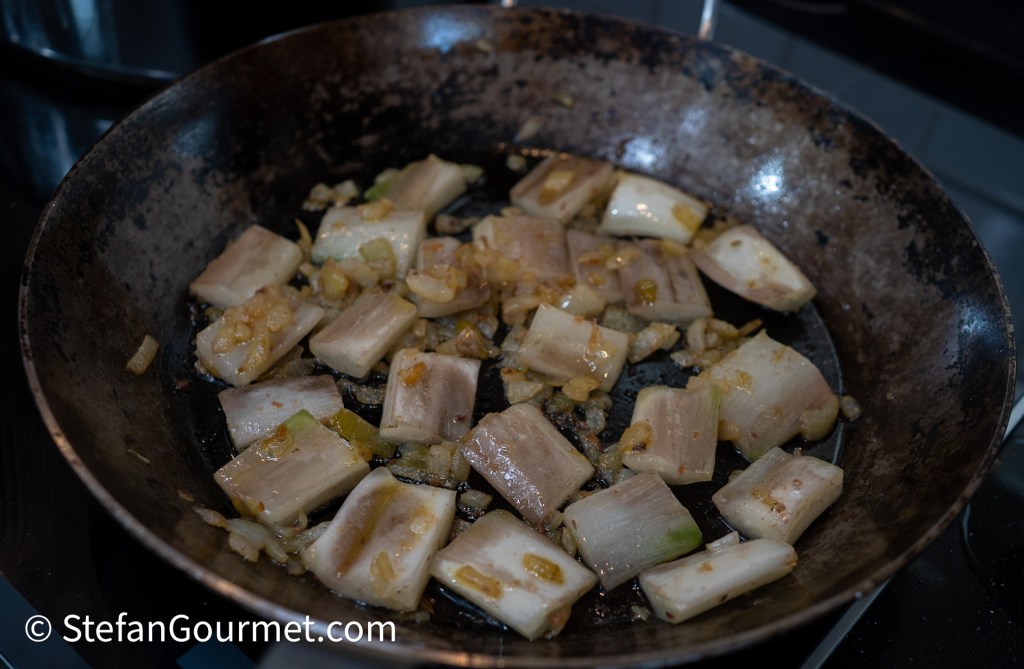 Sautéed pieces of leeks and onions in a frying pan on a stovetop.