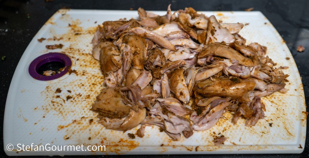 Shredded cooked chicken seasoned with spices on a white cutting board.