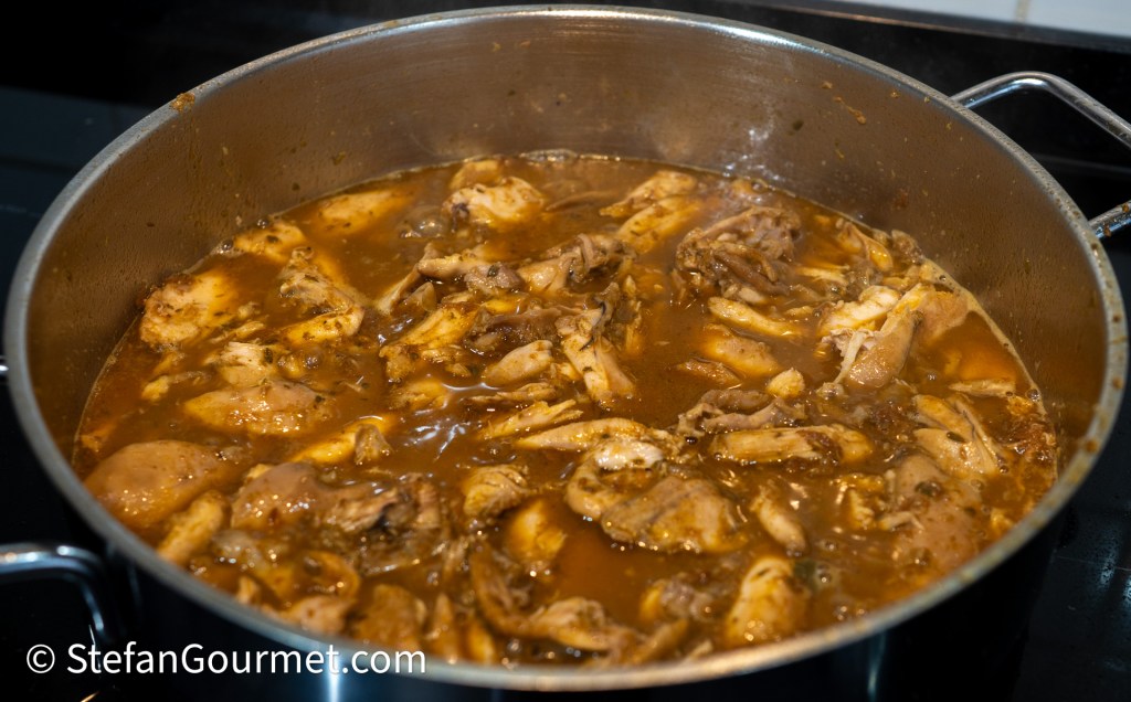 A pot filled with chicken pieces simmering in a rich brown sauce, indicating a savory dish in preparation.