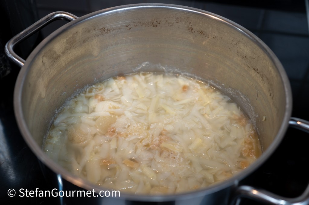 A large pot filled with boiling water, pasta, and seasonings, simmering on a stovetop.