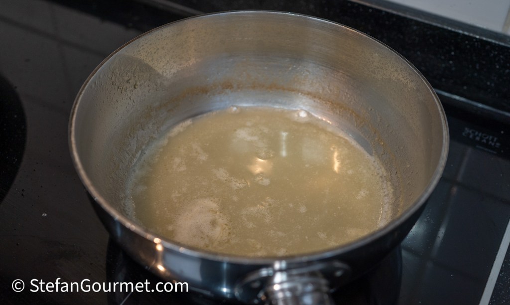 A stainless steel pot on a stovetop with a light brown liquid simmering inside.