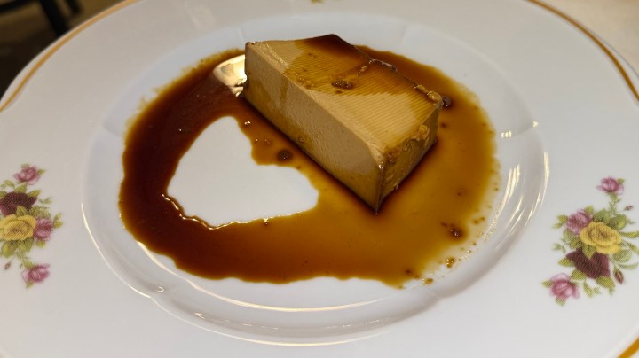A slice of caramel flan served on a decorative plate with a rich caramel sauce.