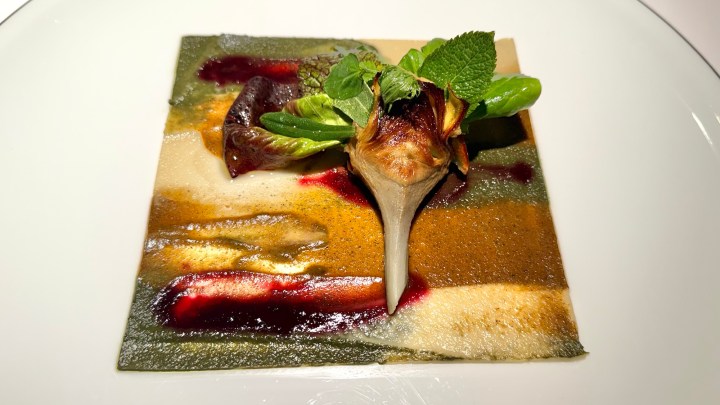 A visually appealing gourmet dish featuring vibrant layers of colored sauces and garnished with fresh mint leaves and a unique artichoke presentation.