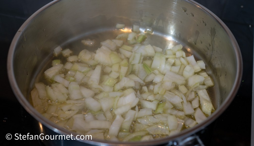 Chopped onions sautéing in a pot with oil.