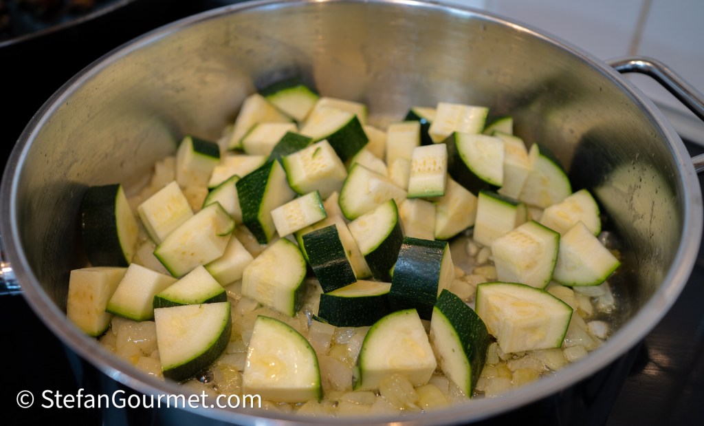 A pot filled with chopped zucchini pieces cooking with onions on a stovetop.