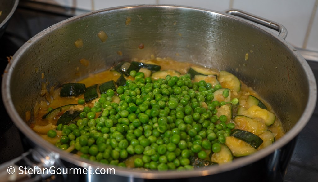 A pot simmering with sautéed vegetables, including sliced zucchini and green peas, on a stovetop.