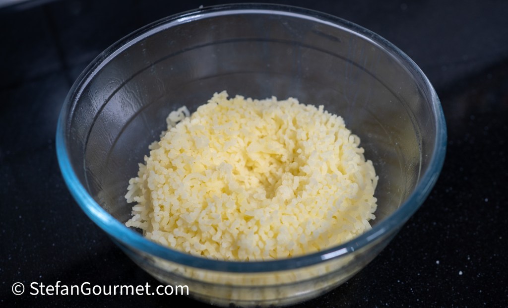 A glass bowl containing fluffy, cooked rice on a black countertop.