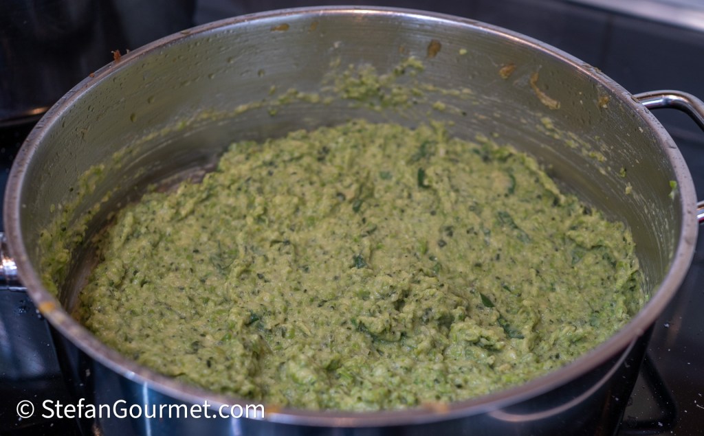 A pot filled with a thick, green, textured mixture, likely a puree or sauce, cooking on a stovetop.