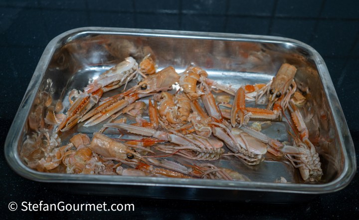 A metal tray filled with cooked langoustines, showcasing their pinkish-brown shells and claws.