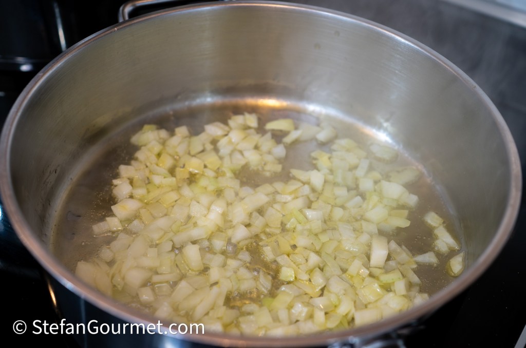 Diced onions sautéing in a stainless steel pot on a stovetop, with steam rising.