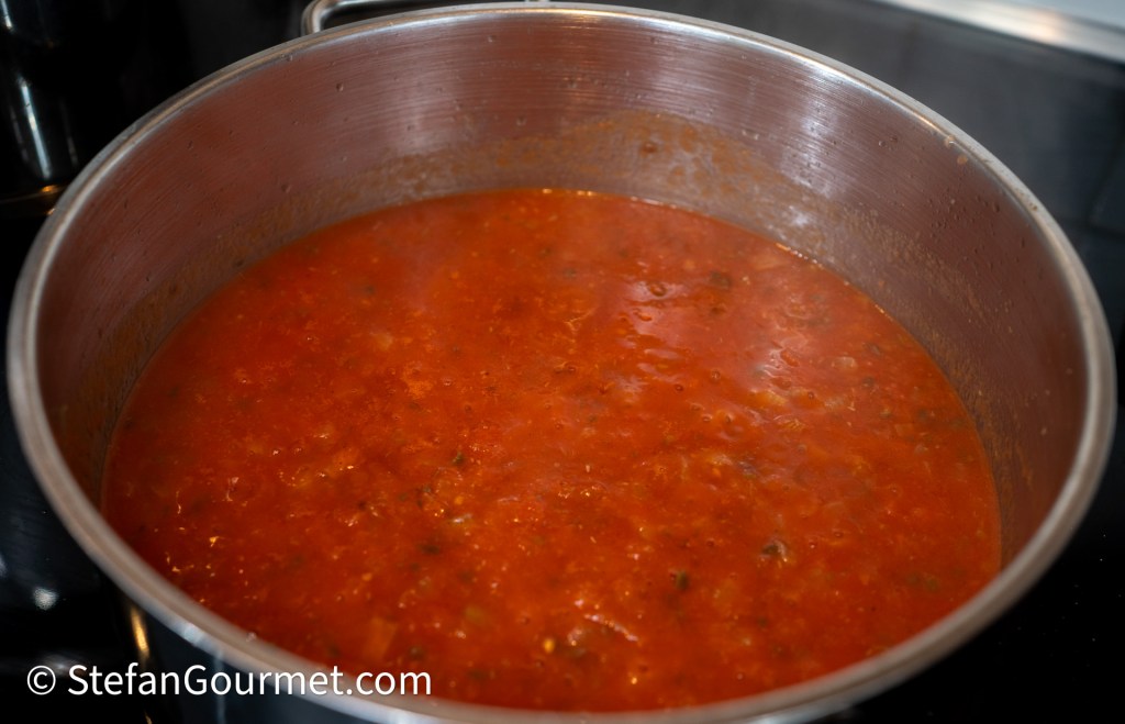 A pot of simmering tomato sauce with herbs on a stovetop.