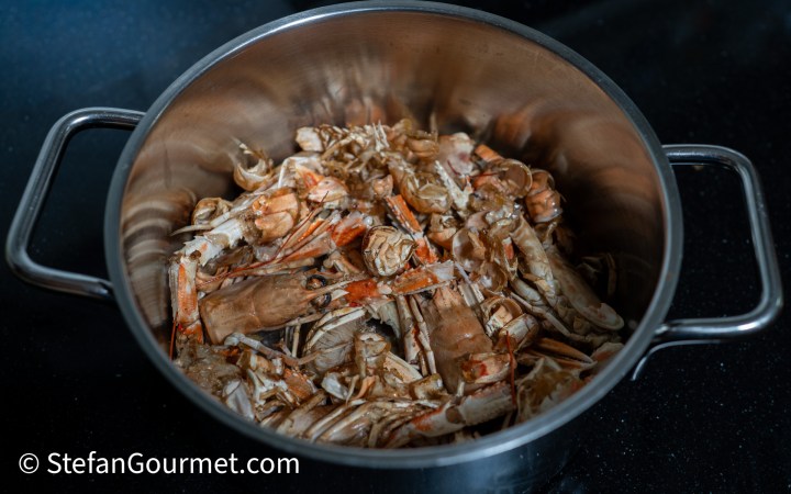 A stainless steel pot filled with crab shells and remnants, showcasing a seafood preparation scene.