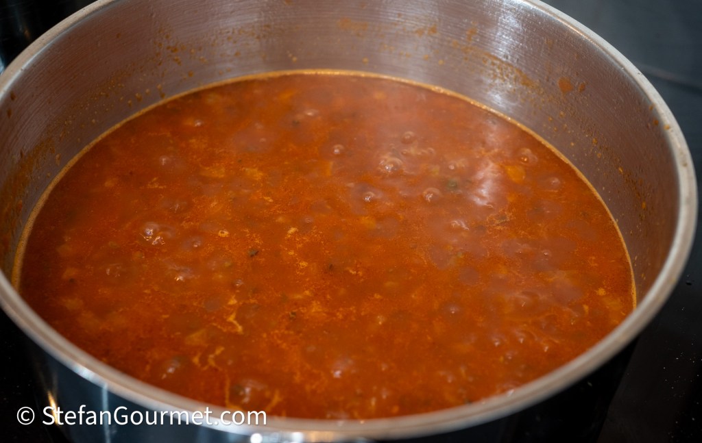 A large pot of bubbling tomato-based sauce cooking on a stovetop.