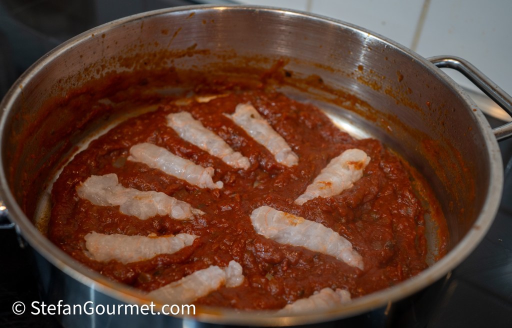 A pot of tomato sauce with slices of seafood placed on top, simmering on a stovetop.