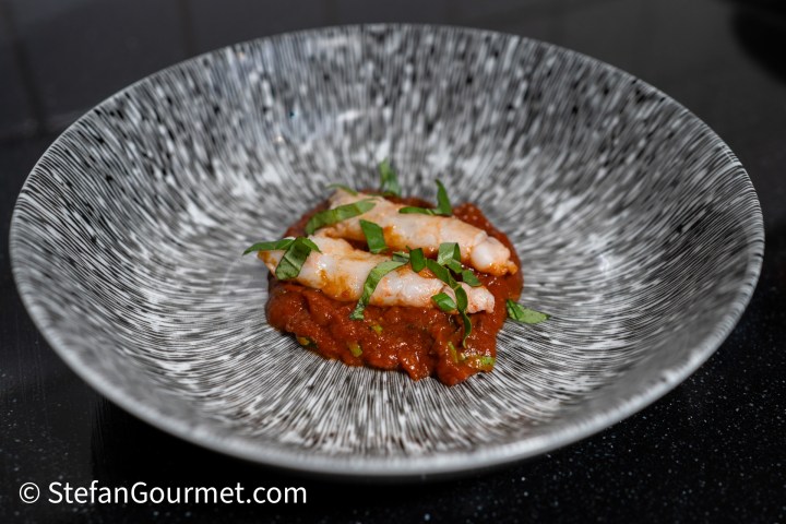 A stylish plate featuring a serving of shrimp on a bed of rich tomato sauce, garnished with fresh basil.
