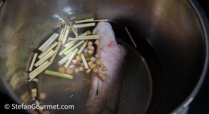 A pot filled with water, featuring a piece of meat and chopped lemongrass.