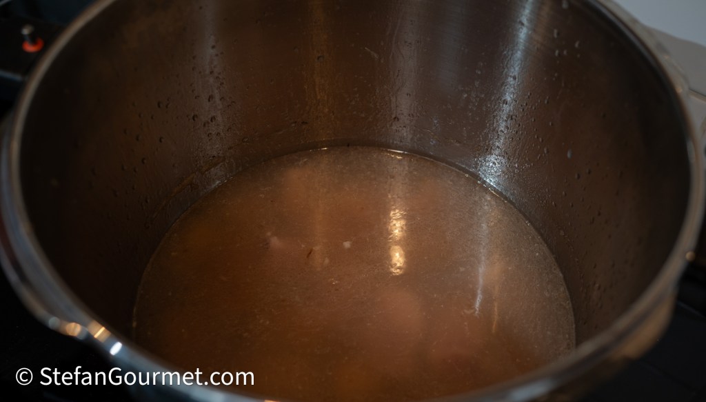 A close-up view of a pot filled with cooking broth, showing steam condensation on the inner walls.