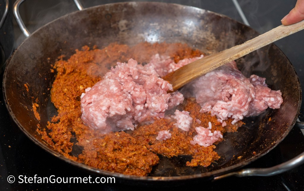 Ground meat being stirred into a pan with spices and sauce, creating steam while cooking.