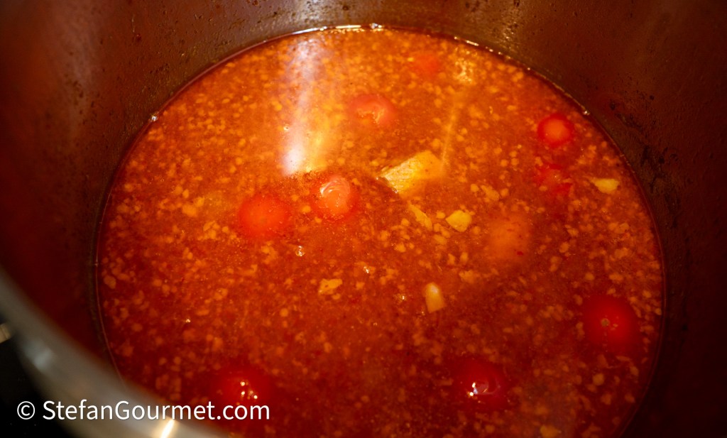 A close-up view of a pot filled with simmering tomato-based soup, featuring pieces of vegetables and spices.