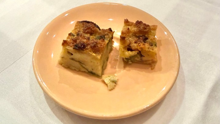 Two pieces of baked egg dish on a pink plate, with a golden brown crust and light green interior, served on a white tablecloth.