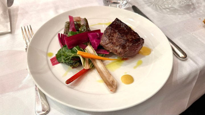 A gourmet plate featuring a perfectly cooked piece of meat alongside a colorful assortment of sautéed vegetables, including greens and chard, drizzled with a light sauce.