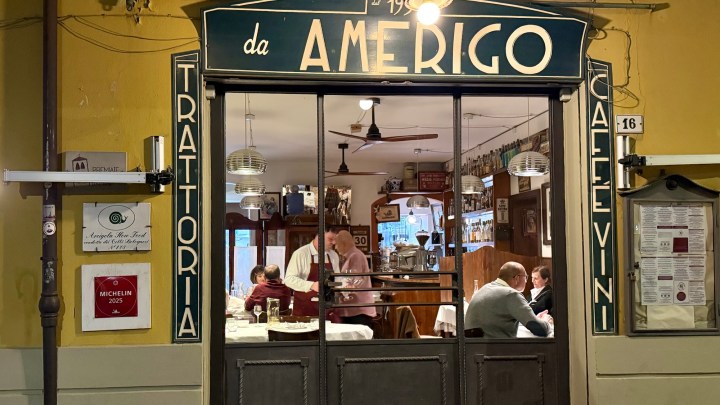 Exterior view of Trattoria da Amerigo, showcasing its entrance with a vintage sign, featuring the words 'da Amerigo' and 'Trattoria', with diners visible inside.