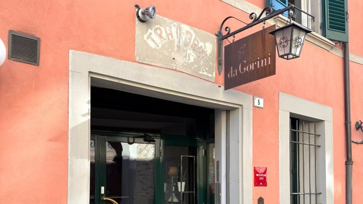 Exterior view of a restaurant named 'da Gorini' with a peach-colored wall and an entrance framed by a gray stone border.