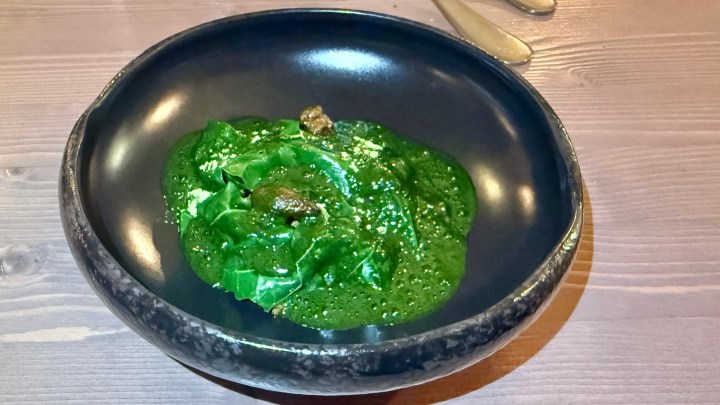 A dark plate containing a vibrant green dish, featuring a creamy textured sauce with small bits of garnish on top.