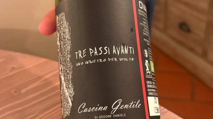 A close-up of a wine bottle label featuring the text 'TRE PASSI AVANTI' and 'Cascina Gentile di Oddone Daniele'. The label has a black background with artistic designs.